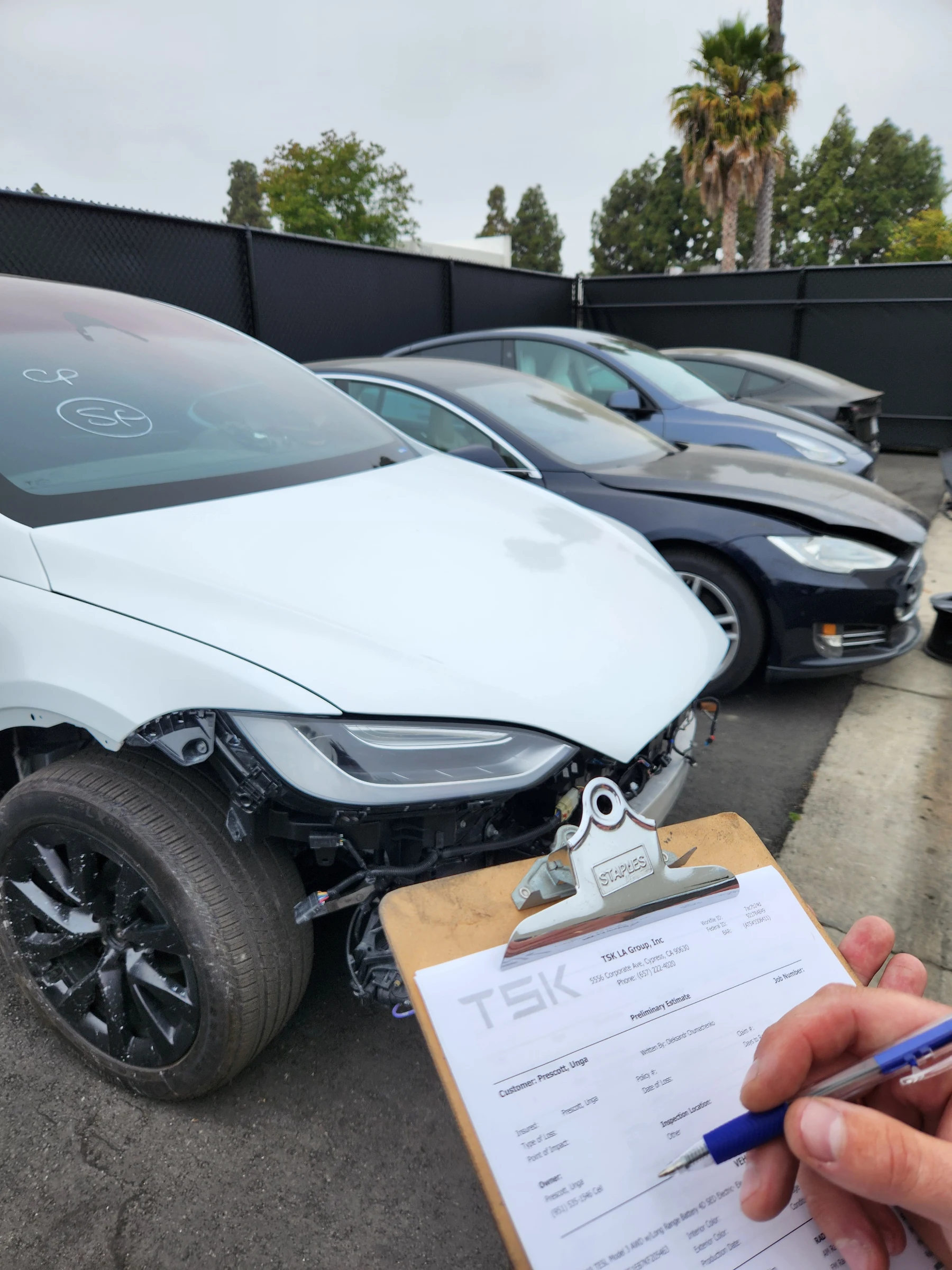 Technician filling in a TSK preliminary estimate beside a Tesla with front-end damage