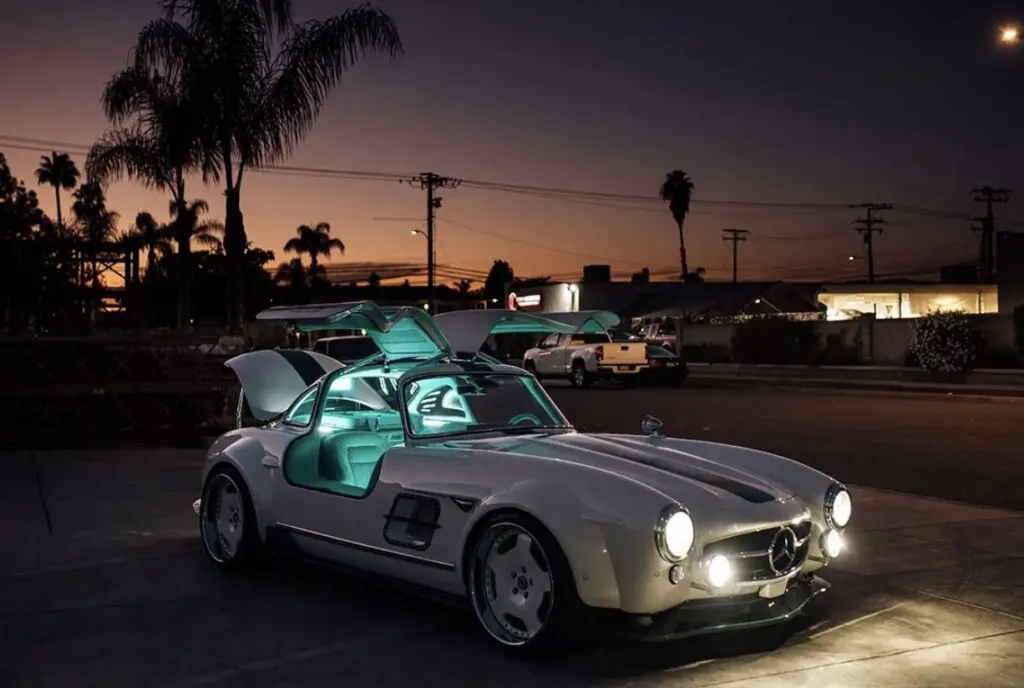 Tesla Gullwing project: white 300SL-style EV with gullwing doors open and a glowing teal interior at dusk