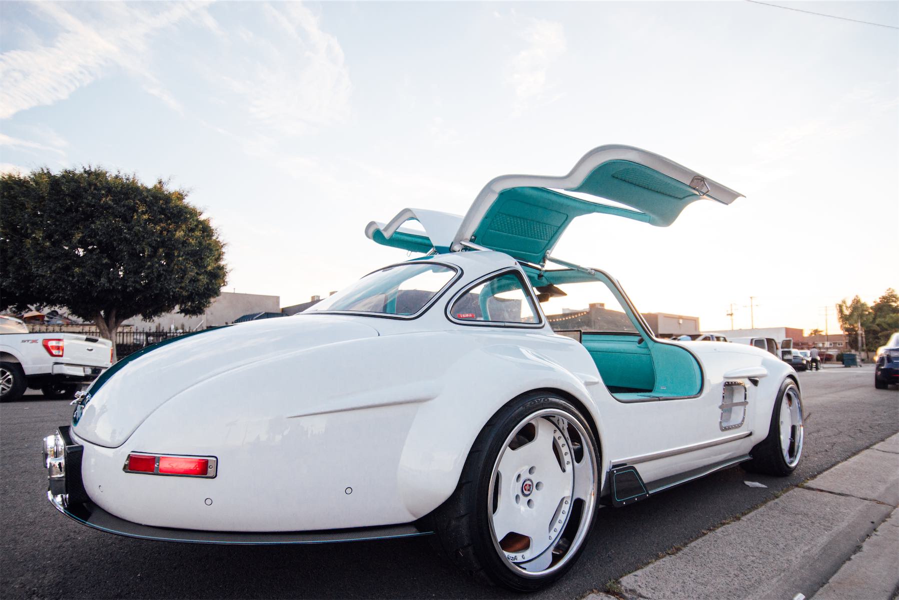 Tesla Gullwing project: white 300SL-style EV with teal interior and doors open, curbside at sunset