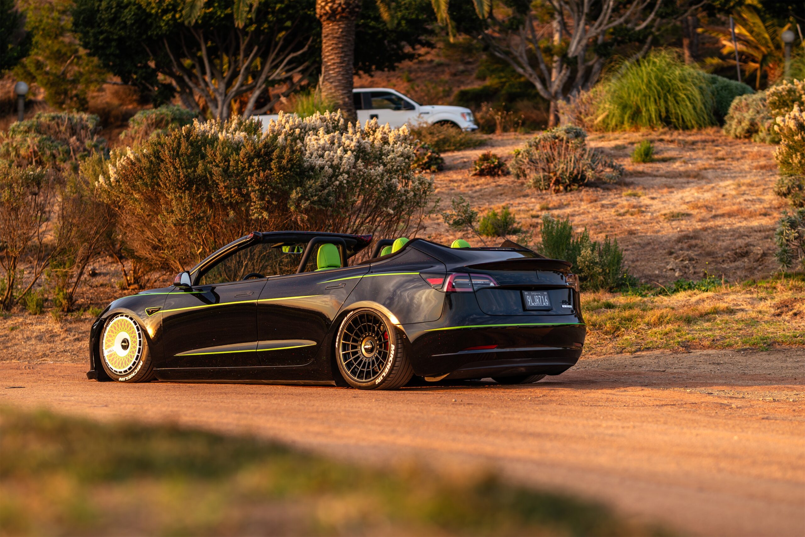 Roofless Tesla project: slammed black Tesla Model 3 convertible on a dirt road at golden hour