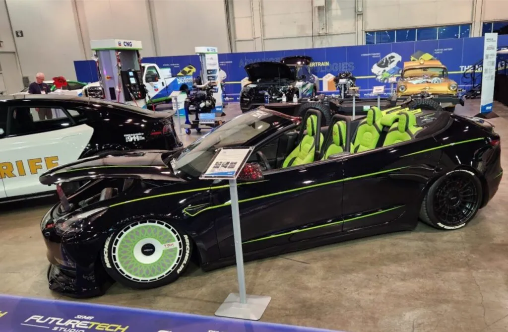 Roofless Tesla project: black Tesla Model 3 convertible with green interior and custom wheels at an indoor auto show