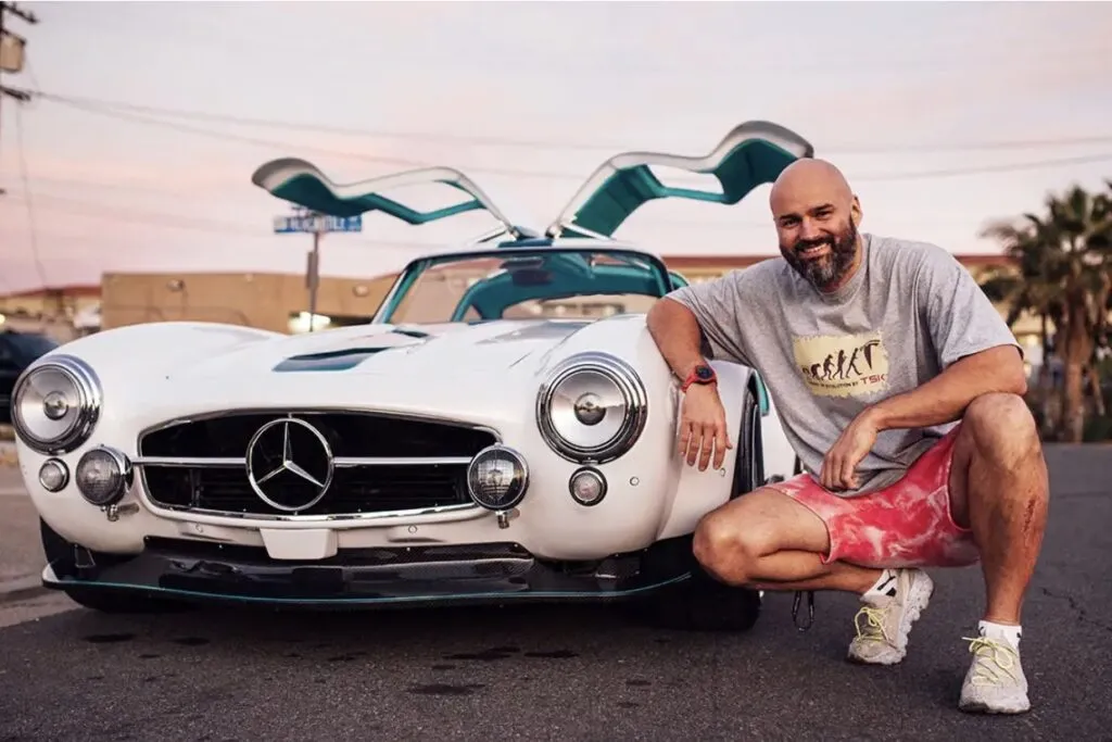 Tesla Gullwing project: smiling man kneeling beside the white 300SL-style EV with its gullwing doors open