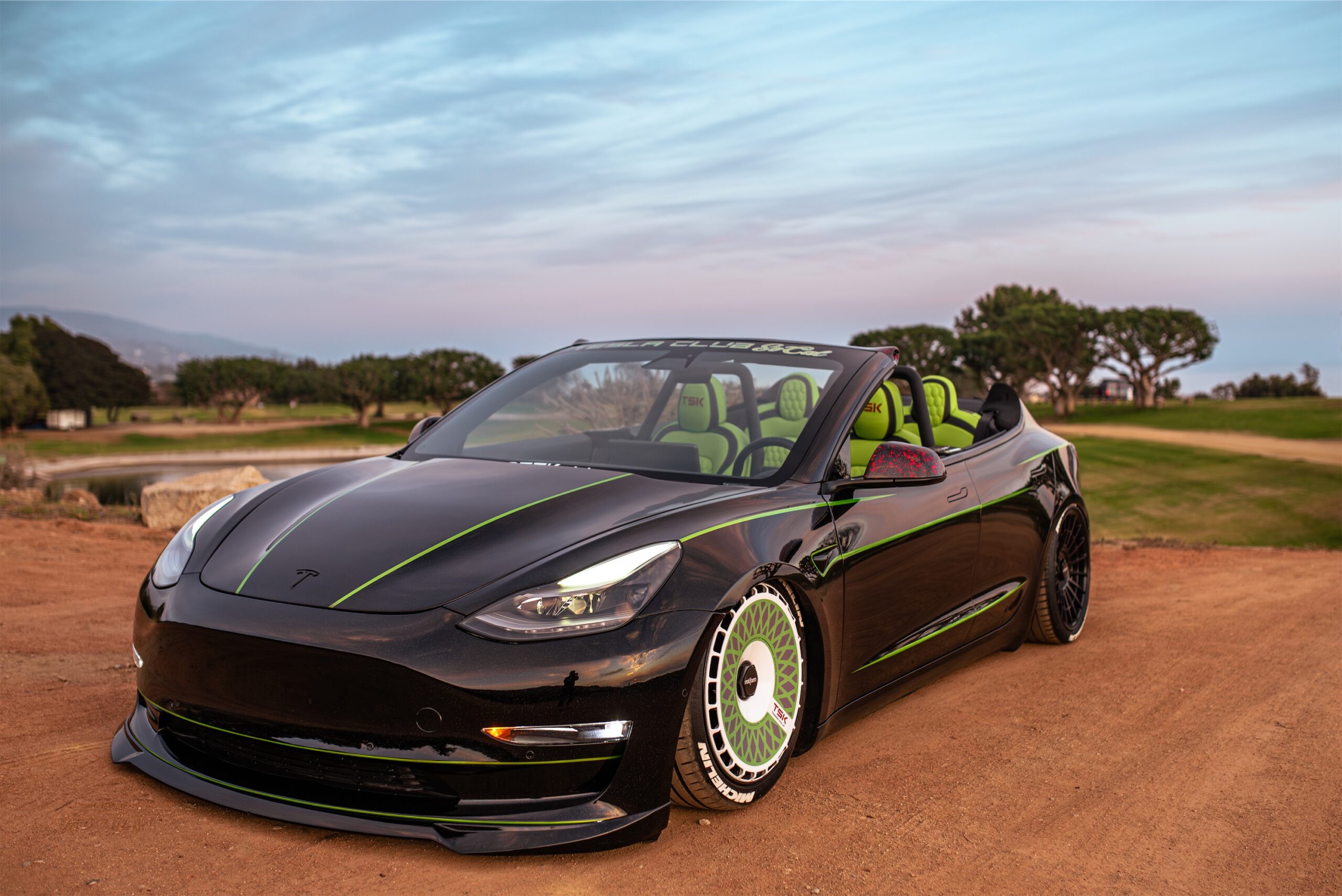 Roofless Tesla project: black Tesla Model 3 convertible with green stripes and roll bar on a dirt lot