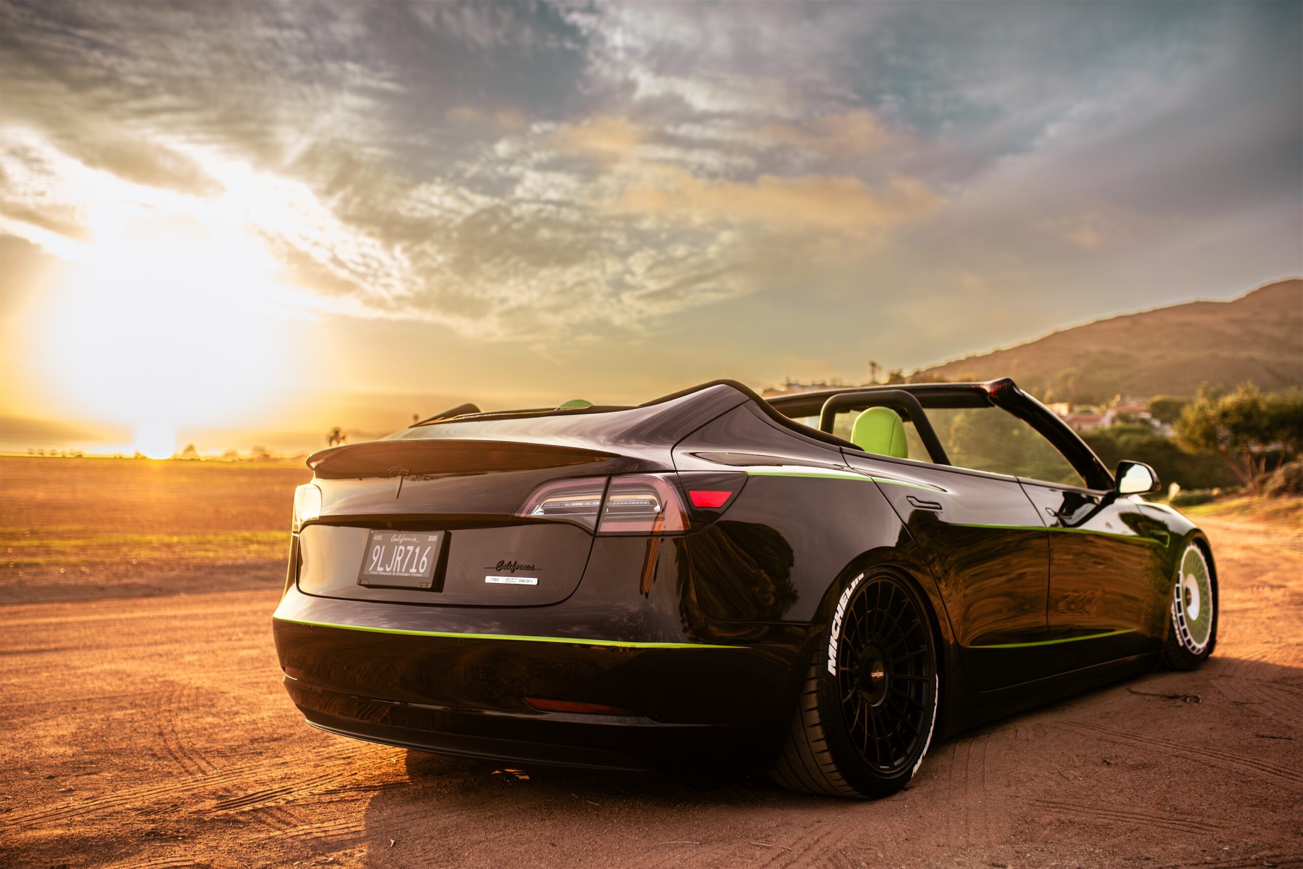 Roofless Tesla project: open Tesla Model 3 with green accents on dirt at sunset