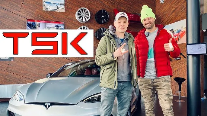 Two men posing beside a silver Tesla Model S inside TSK showroom with wheel displays