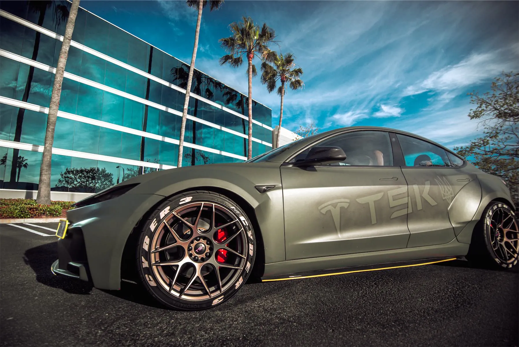 Cyber 3 project: matte green Model 3 widebody with bronze wheels by a glass office building