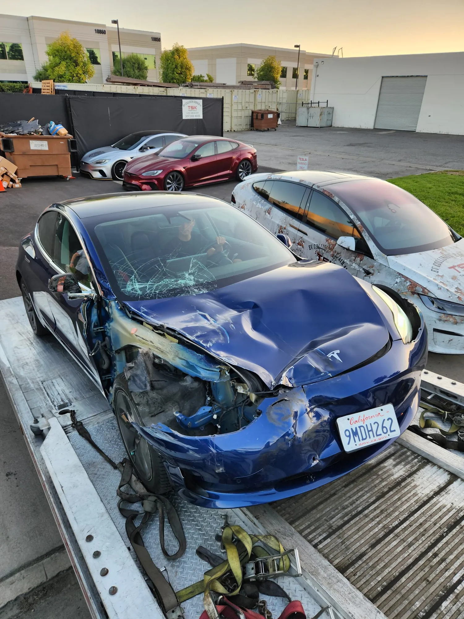 Blue Tesla Model 3 with front-end collision damage on flatbed at TSK shop