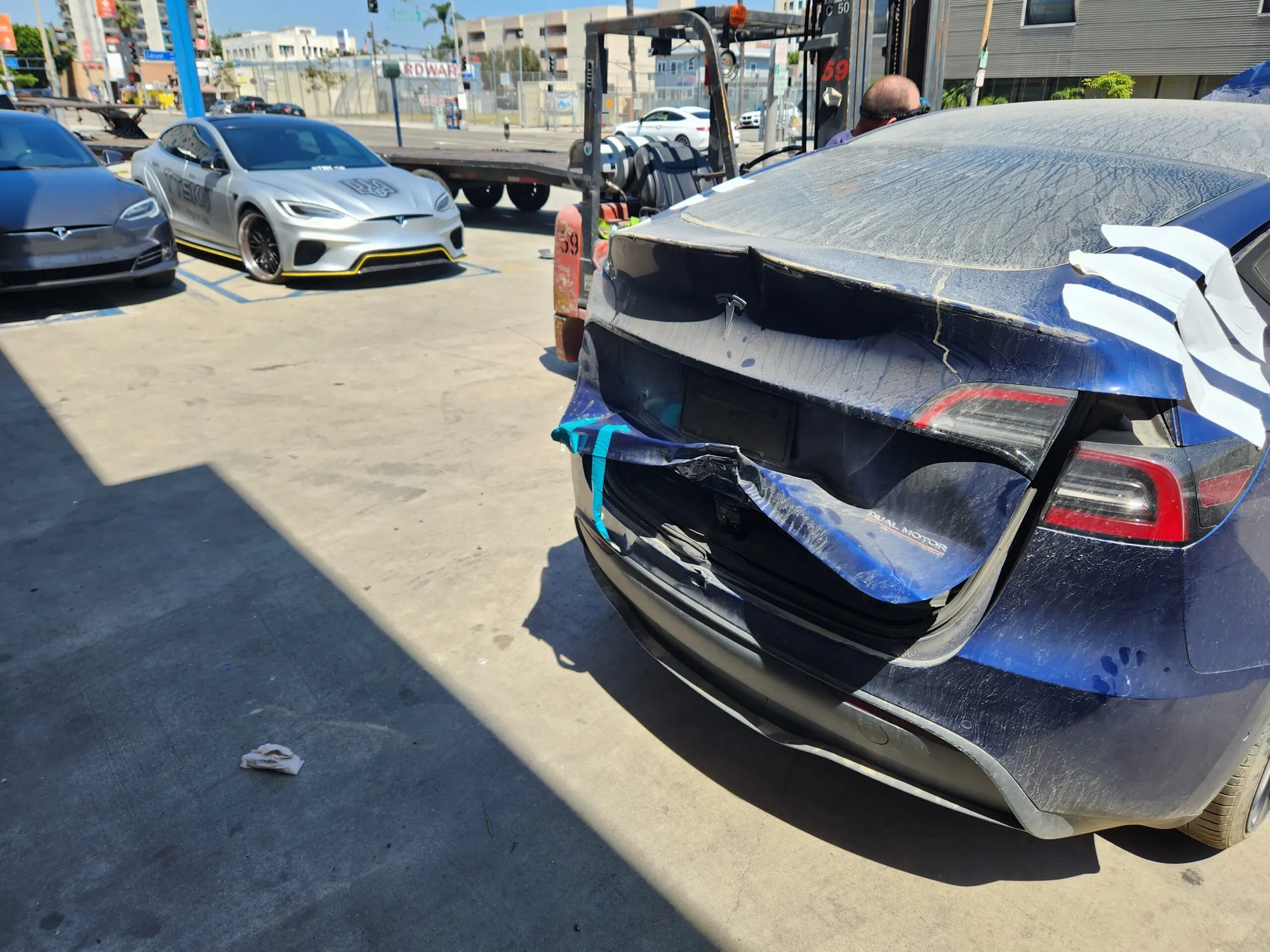 Blue Tesla Model 3 with damaged rear bumper and trunk at TSK body shop