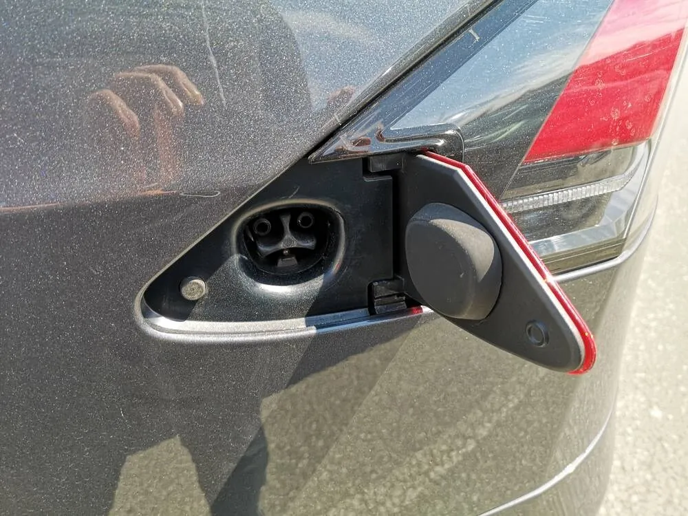 Open Tesla charging port with door swung out, taillight visible in background