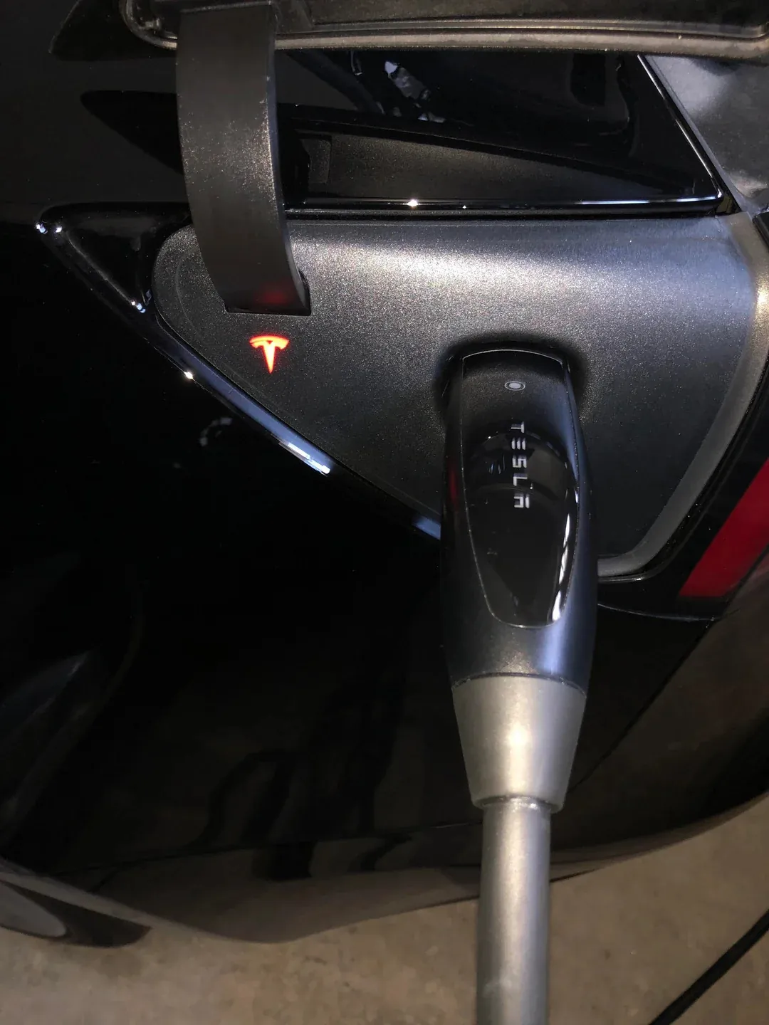 Tesla charging port with red indicator light and connector plugged in at night