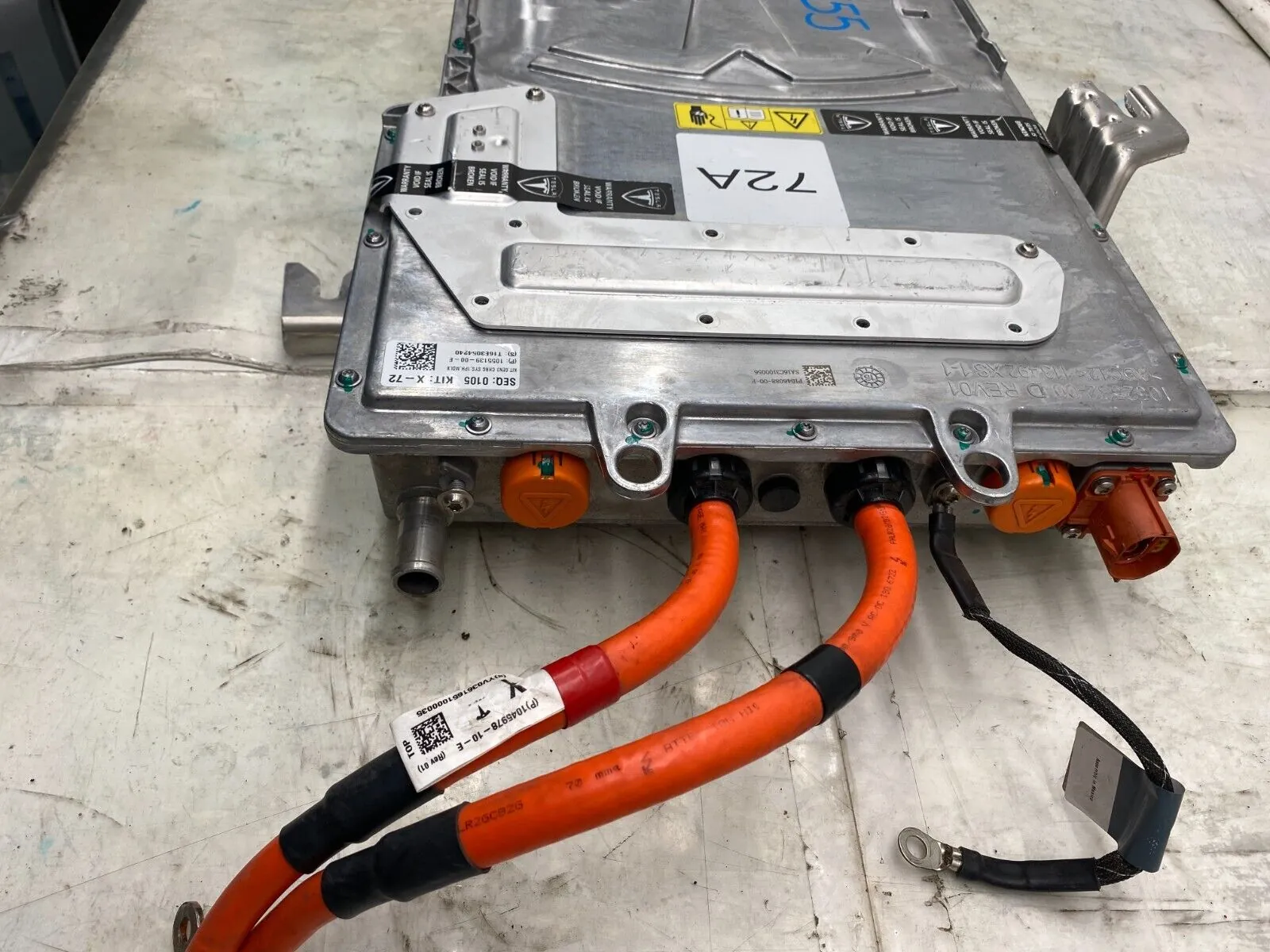Tesla onboard charger unit with orange high-voltage cables on repair shop workbench