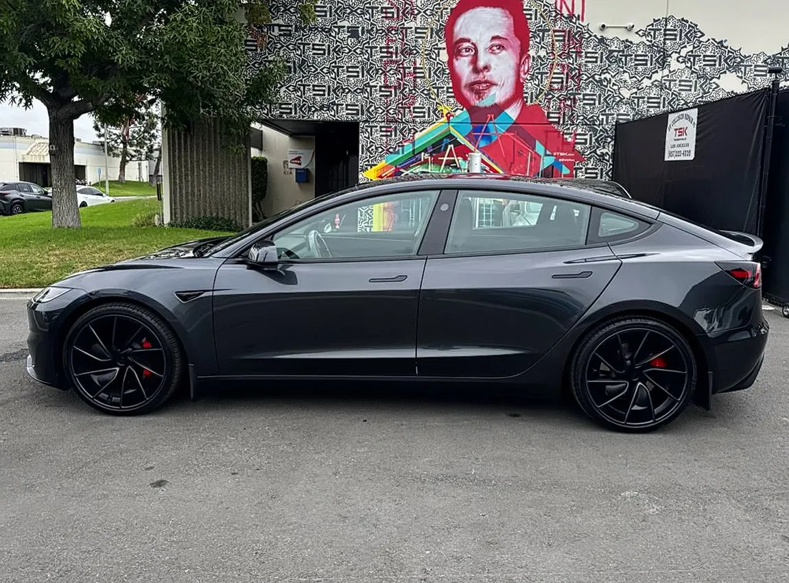 Black Tesla Model 3 parked outside TSK EV collision repair shop with mural backdrop