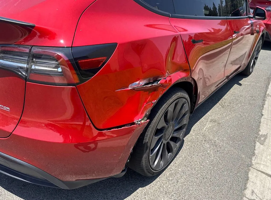 Red Tesla Model Y rear quarter panel damage with scraped paint before collision repair