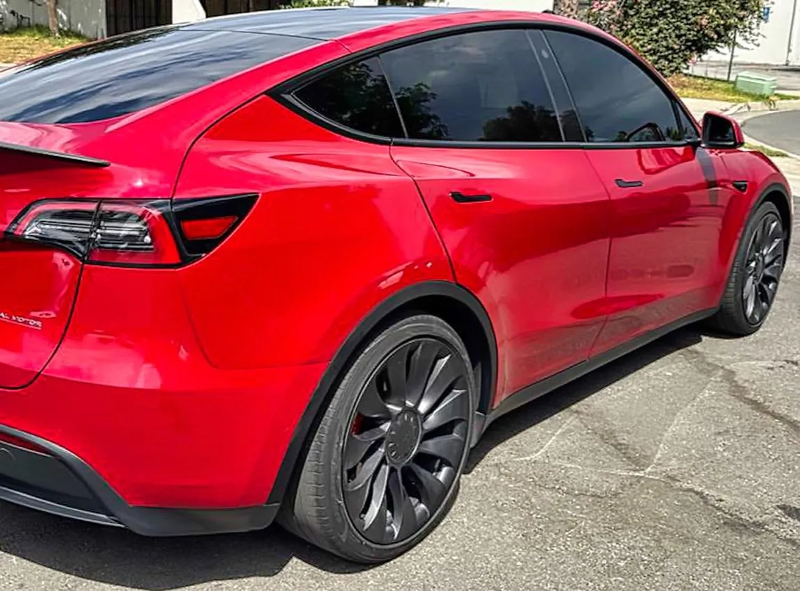 Red Tesla Model Y rear quarter view showing repaired panel and black alloy wheel