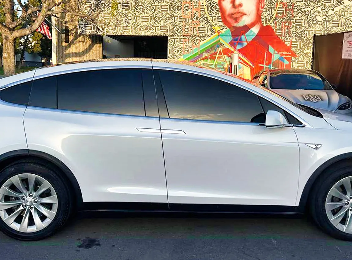 White Tesla Model X side profile parked outside TSK EV Collision Repair shop