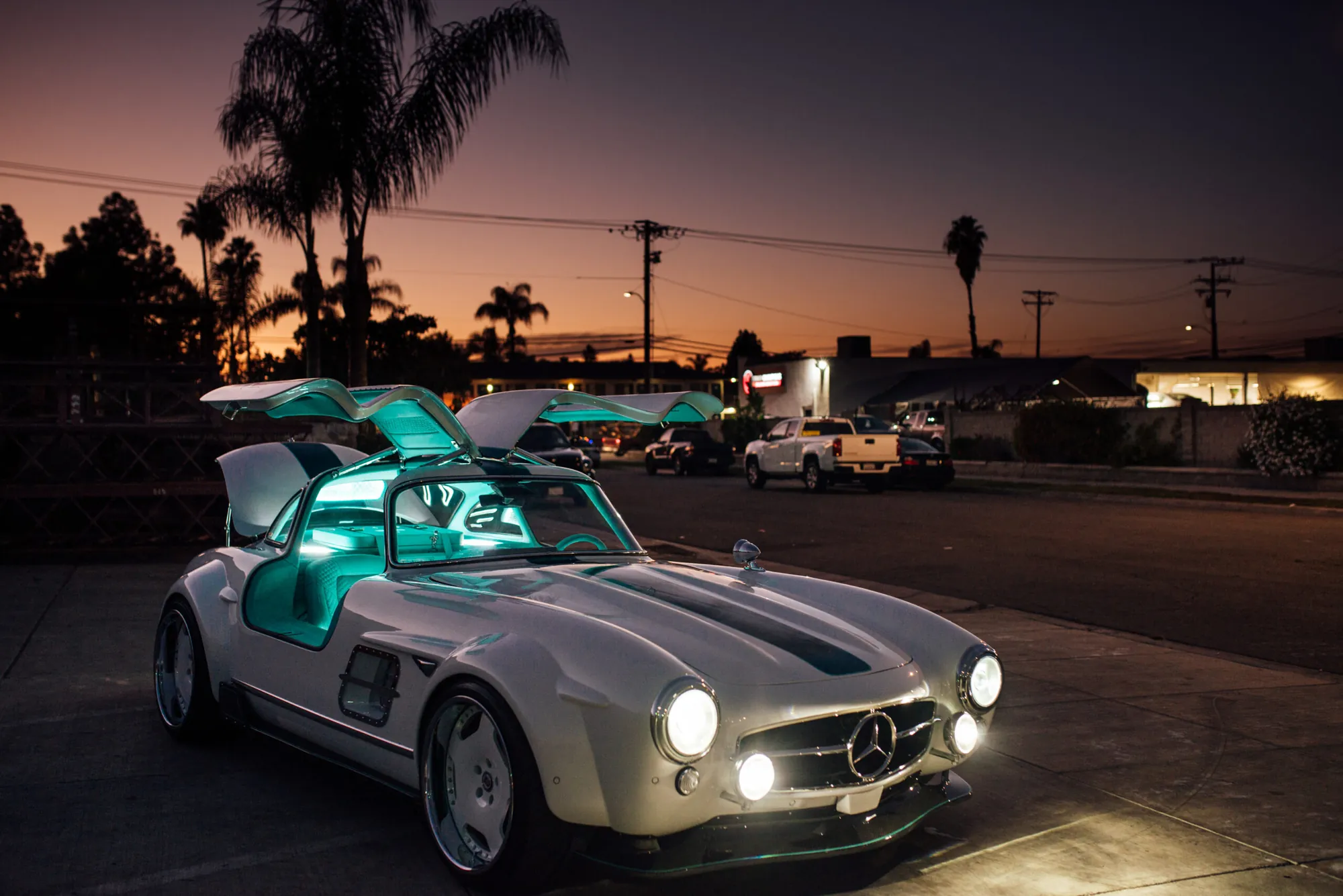 Tesla Gullwing project: white 300SL-style EV with its doors open and teal interior lighting at dusk