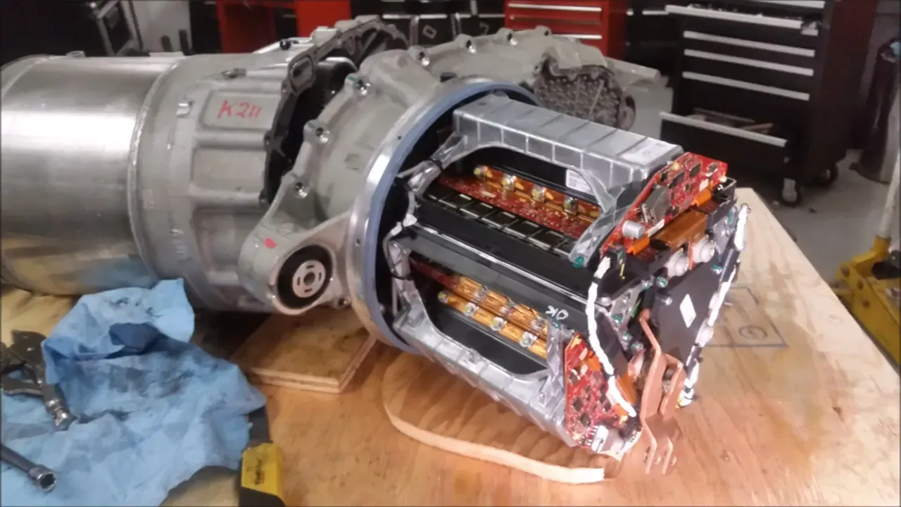 Disassembled Tesla drive unit exposing internal power electronics and inverter boards on workbench