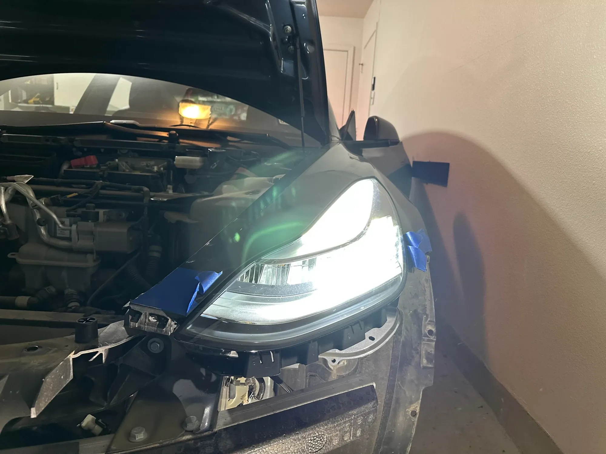 Illuminated headlight installed on car during repair, front fender taped for protection