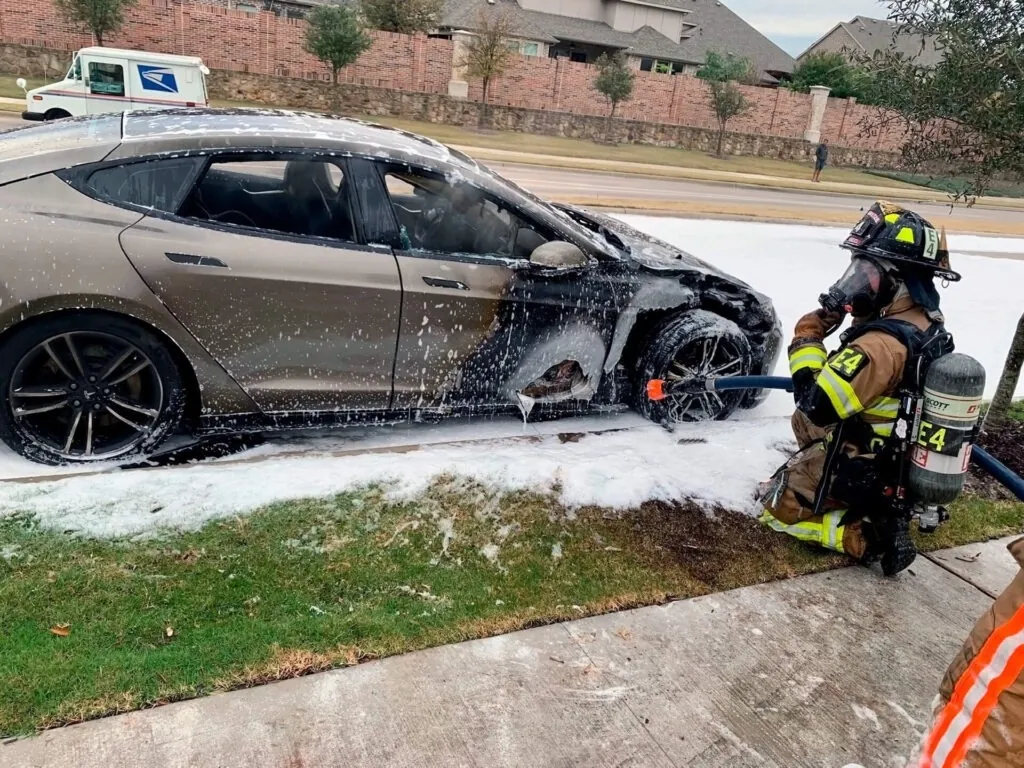 Firefighter applying foam to smoldering Tesla Model S rear after roadside battery fire