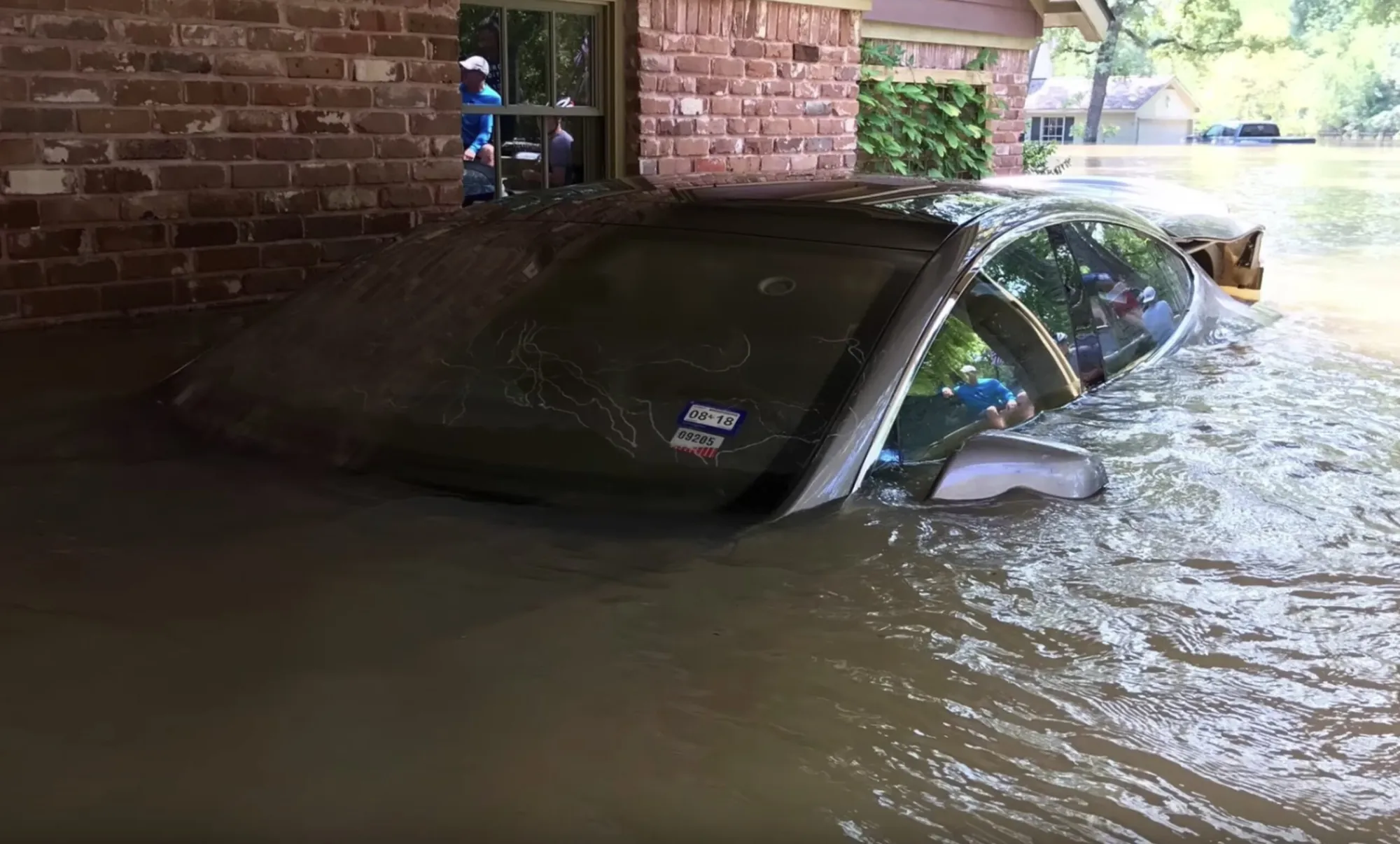 Sedan nearly submerged in floodwater outside brick home, needing Tesla flood recovery service