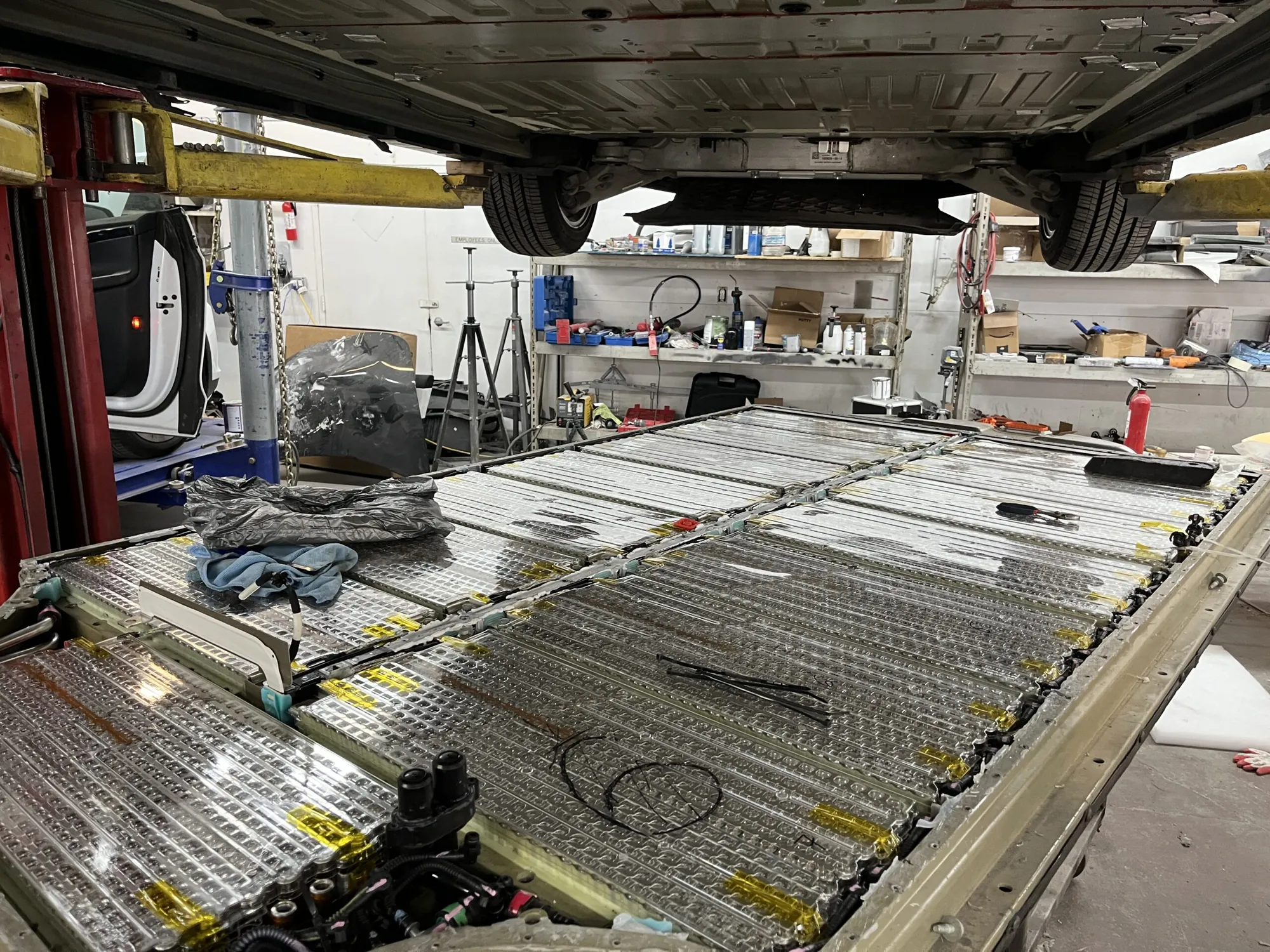 Exposed Tesla high-voltage battery pack under vehicle lift during repair at TSK Cypress