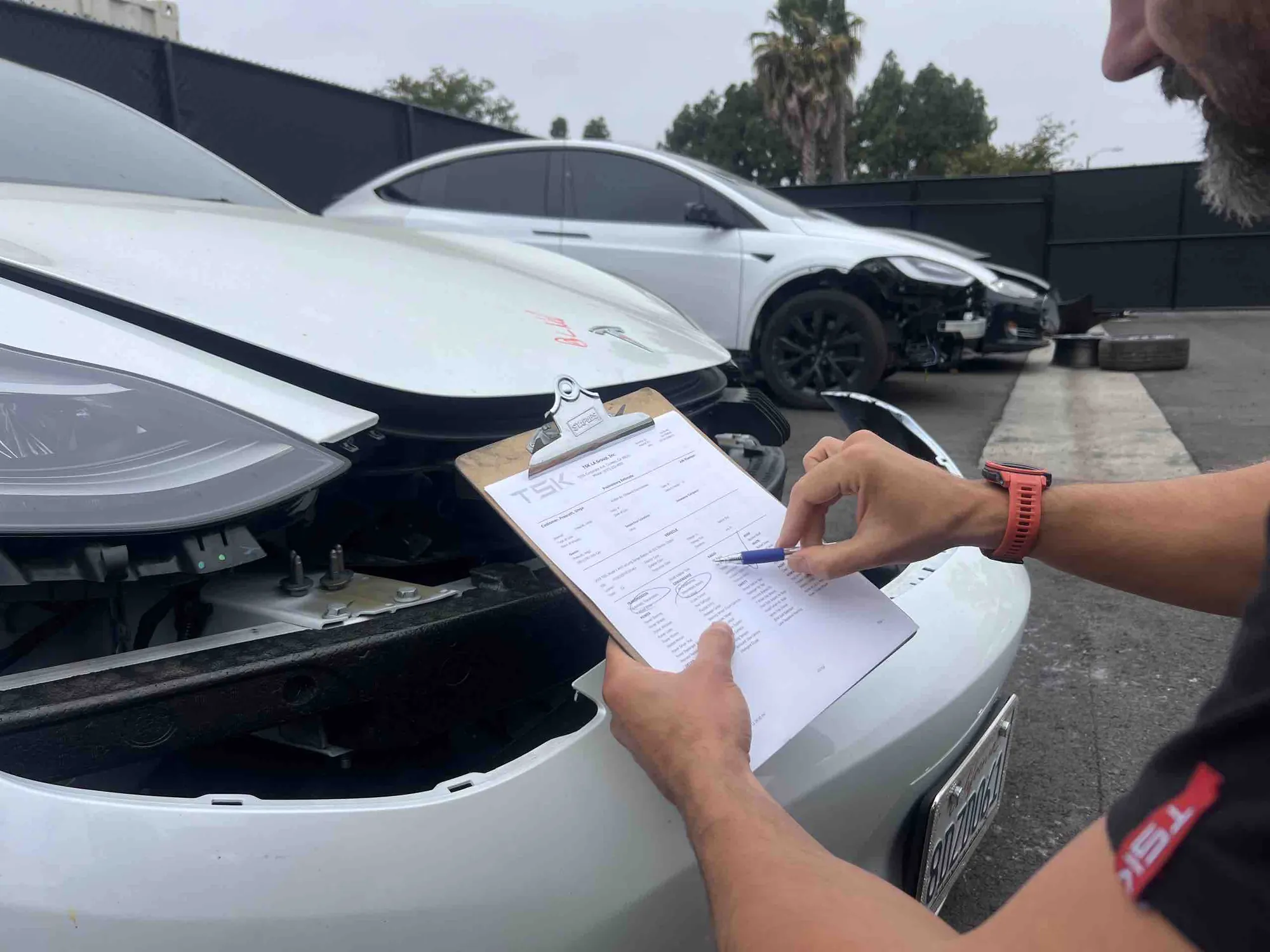 Technician inspecting Tesla Model 3 front bumper damage on TSK inspection checklist in Irvine