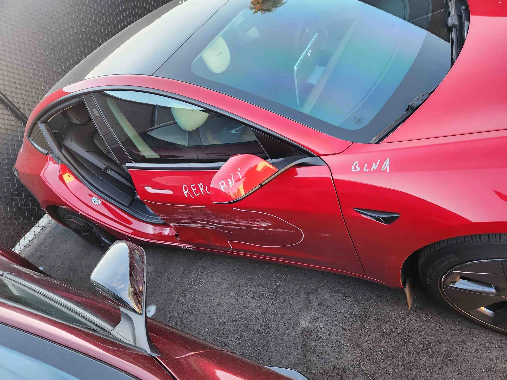 Red Tesla Model 3 with dented front door and marked damage before repair in Irvine