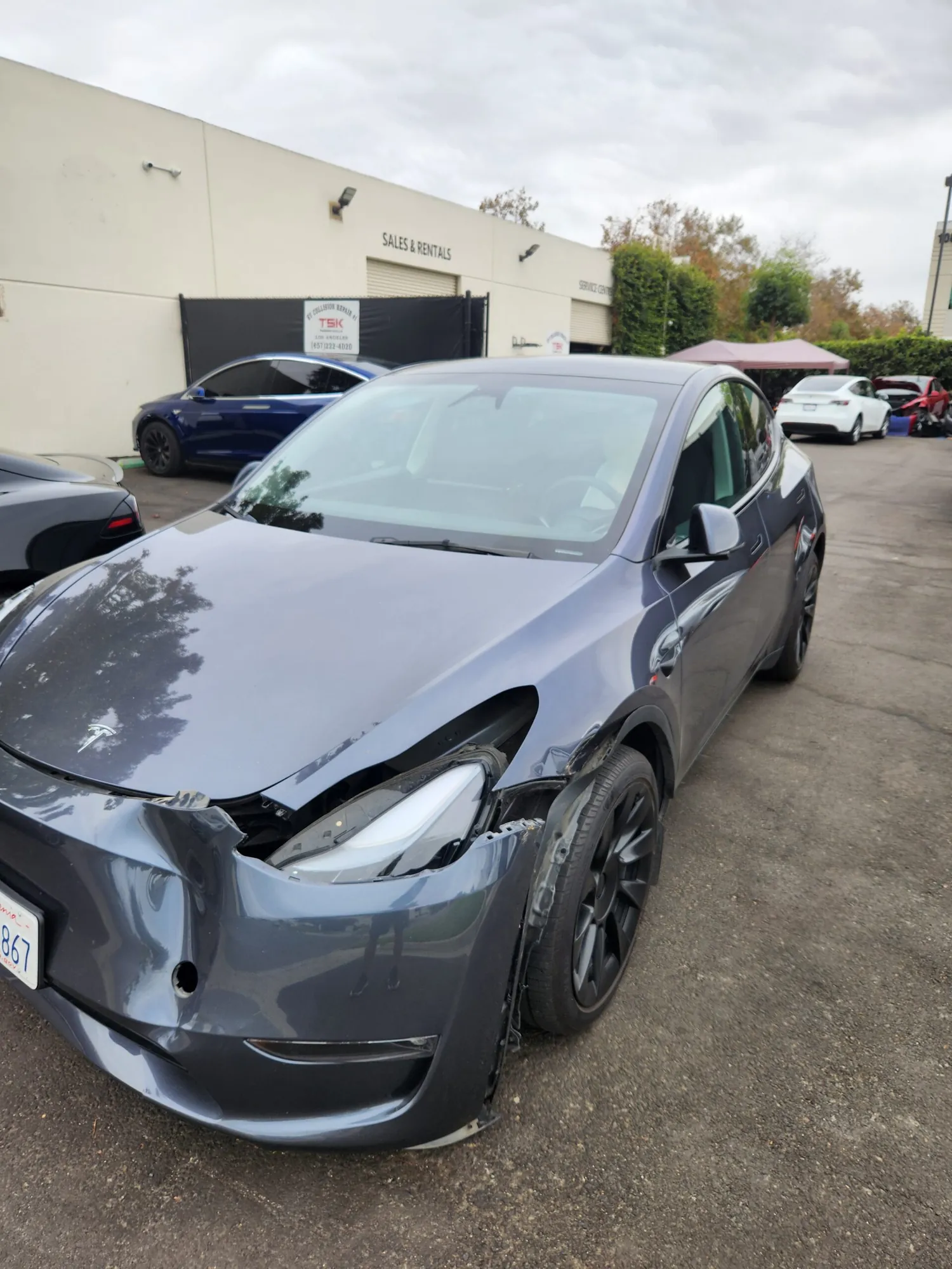 Gray Tesla Model 3 with damaged front bumper and headlight at TSK collision repair lot