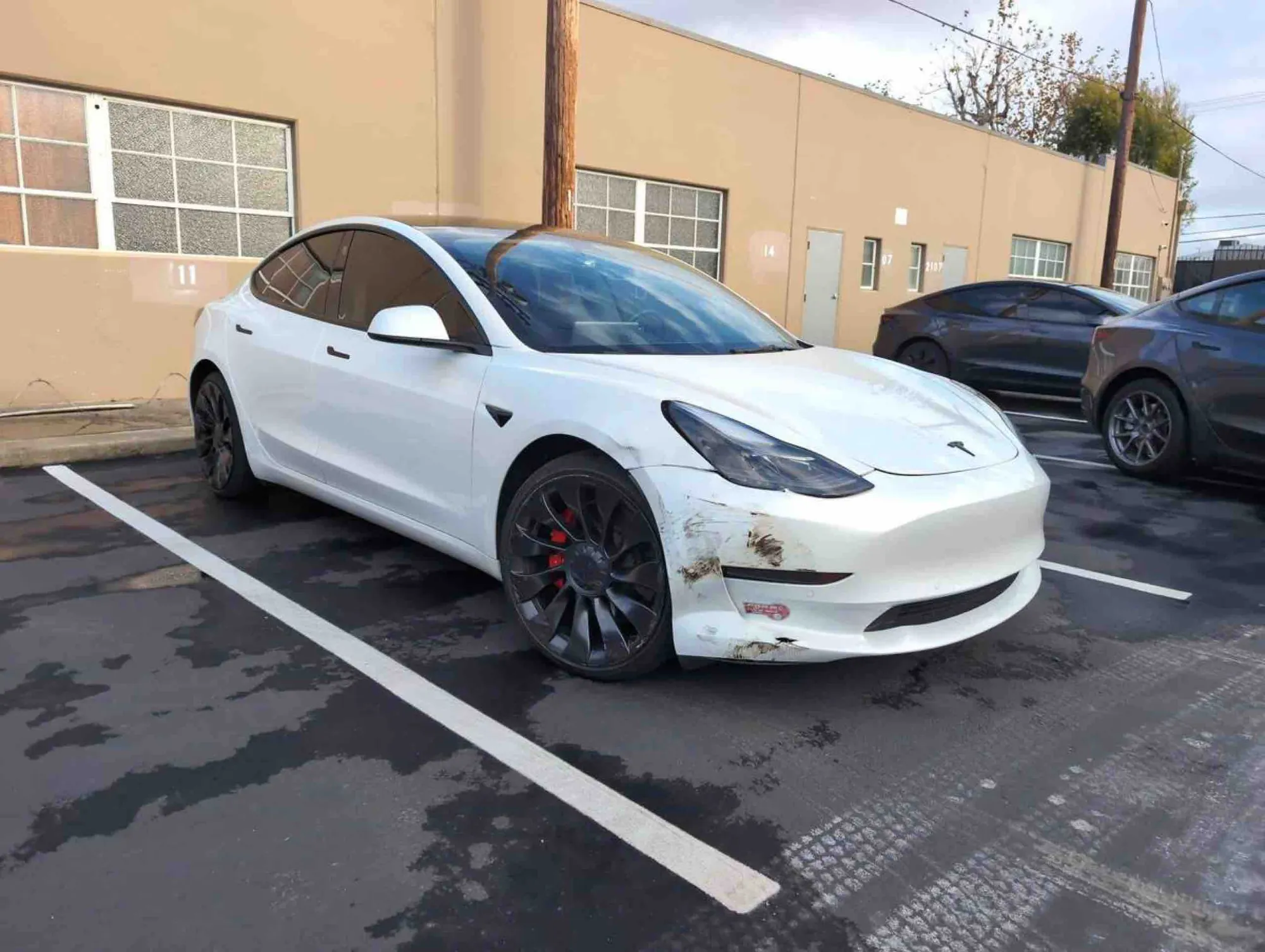 White Tesla Model 3 with front bumper scrapes parked before collision repair in Irvine
