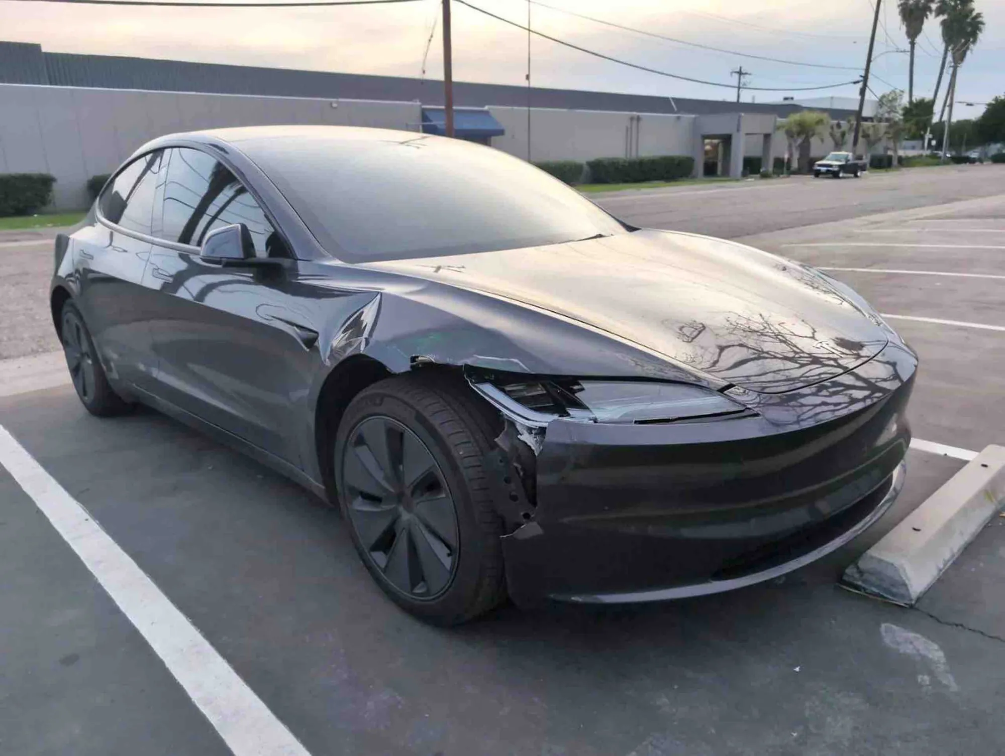 Gray Tesla Model 3 with damaged front bumper and headlight in parking lot
