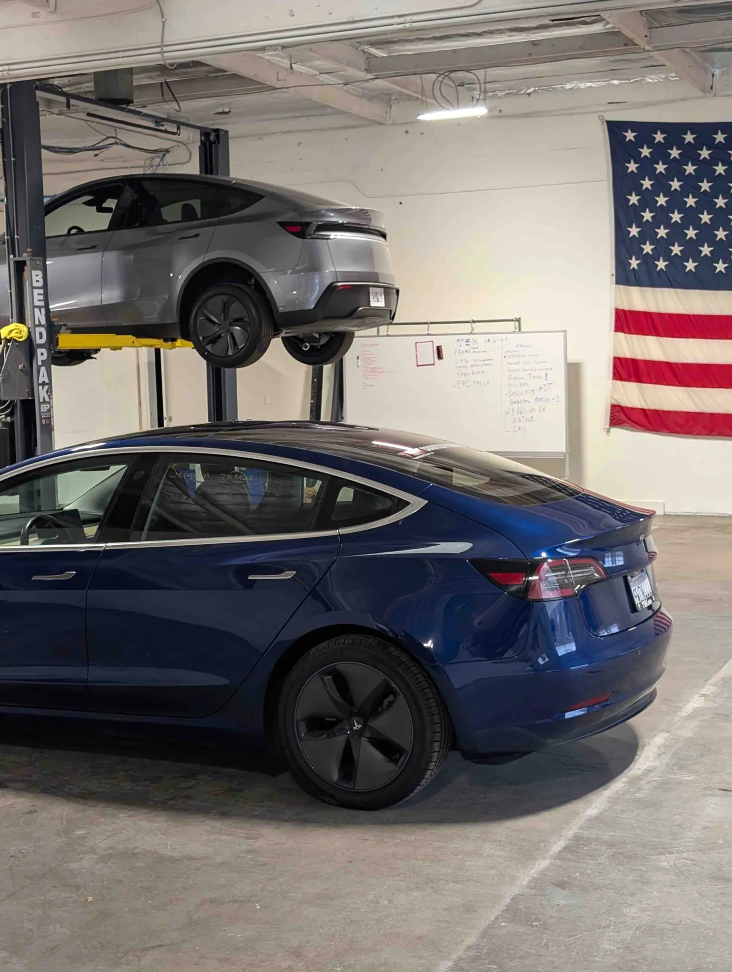 Blue Tesla Model 3 in TSK Irvine shop, gray Model Y on lift above