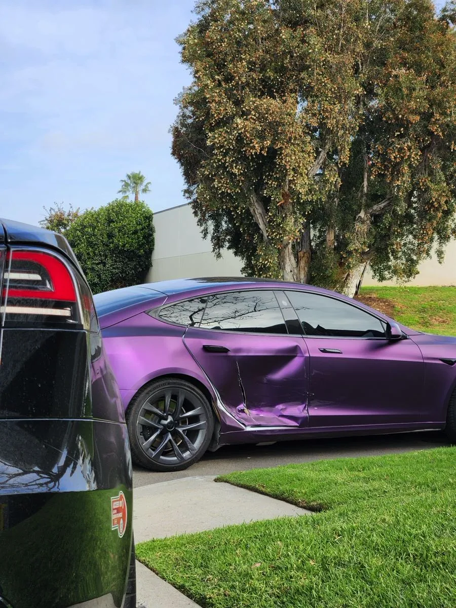 Purple Tesla Model S with crumpled rear door panel before collision repair in Irvine