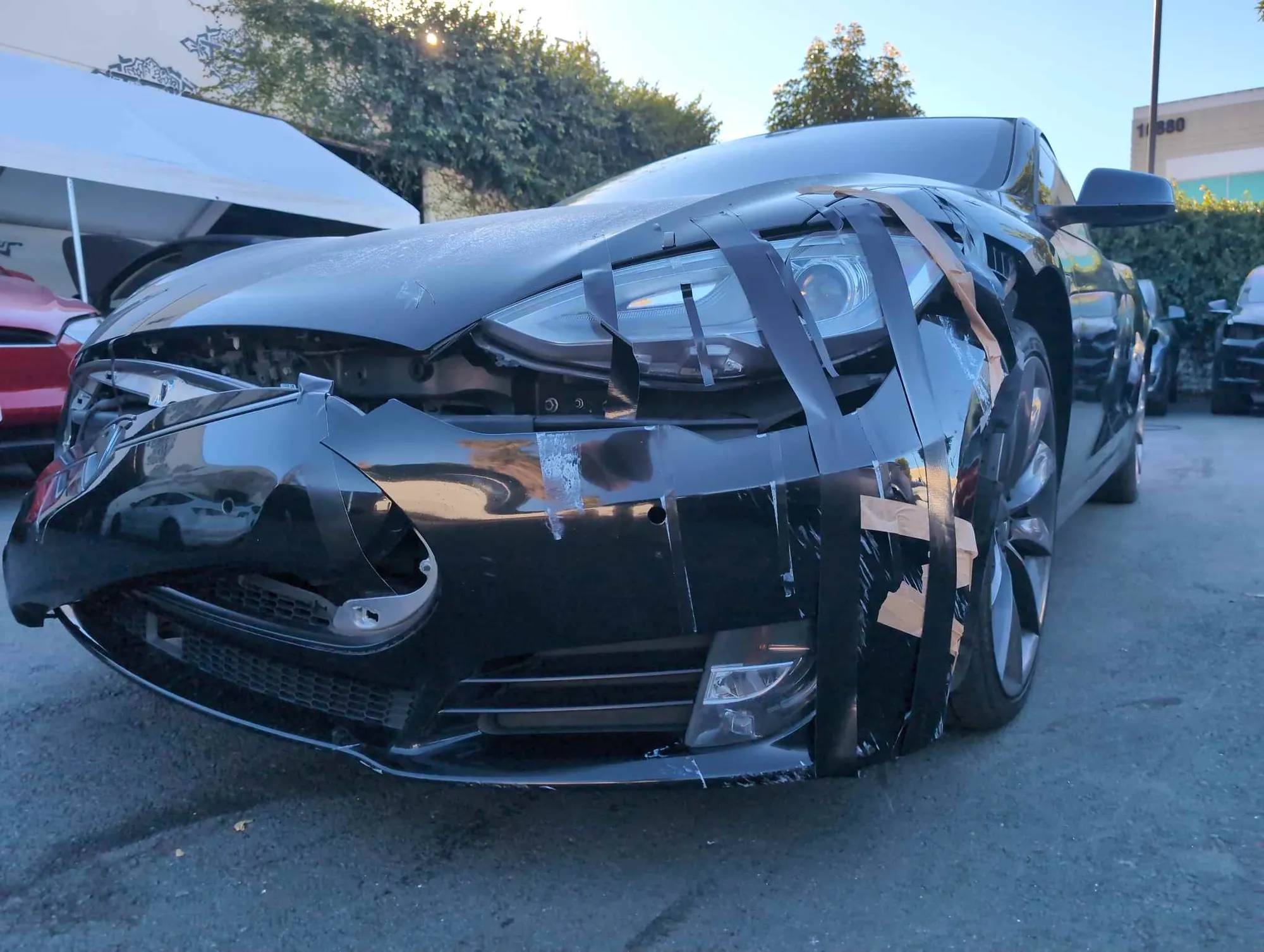Black Tesla Model S with damaged front bumper and headlight taped, awaiting repair in Irvine