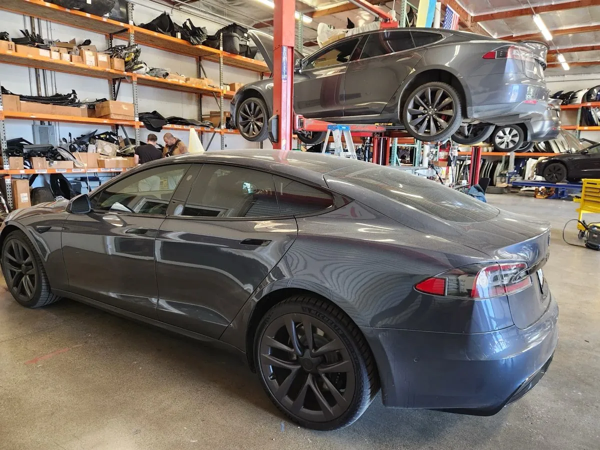 Gray Tesla Model S in TSK Irvine shop, another lifted for repair behind it