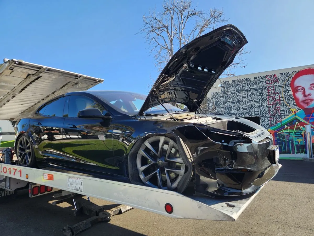 Damaged black Tesla Model S with open hood on flatbed at TSK Irvine