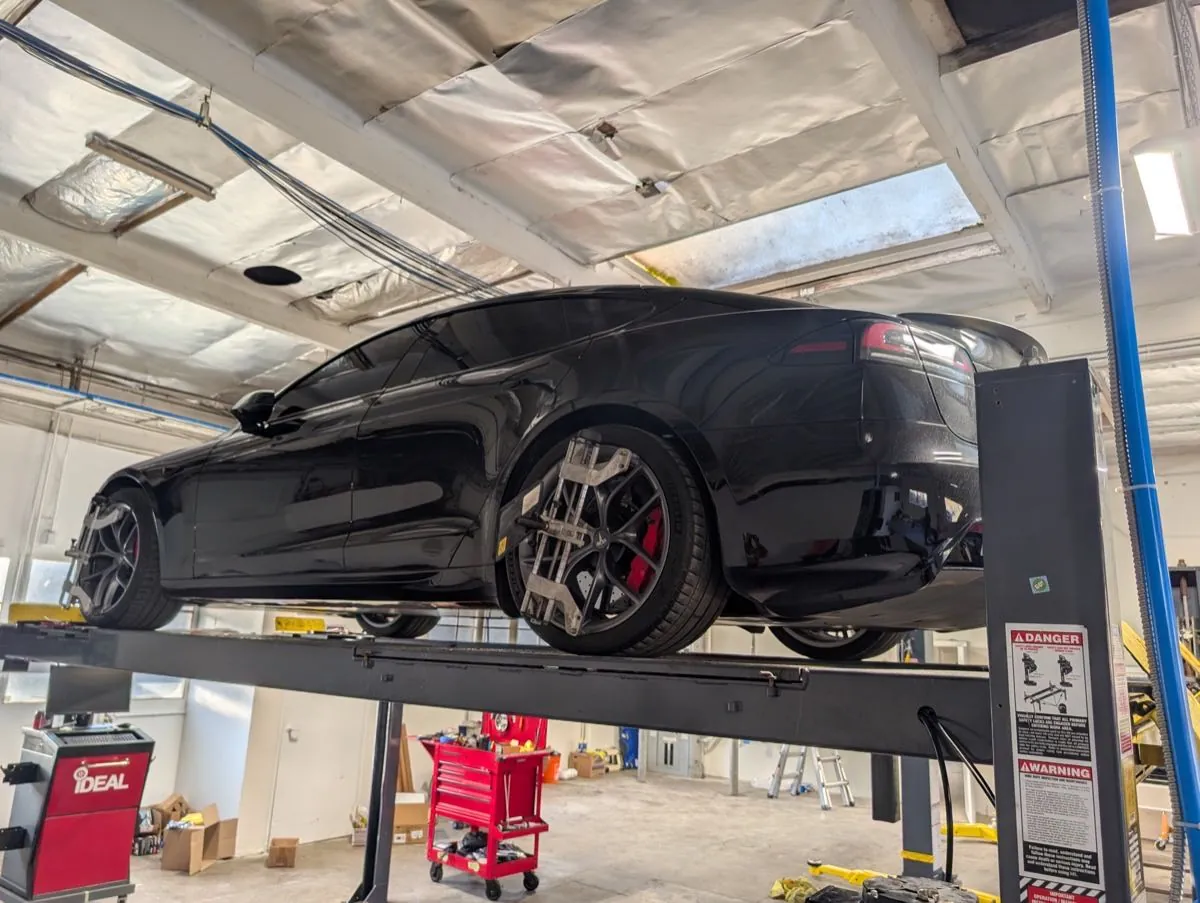 Black Tesla Model S on four-post lift with wheel alignment equipment at TSK Irvine