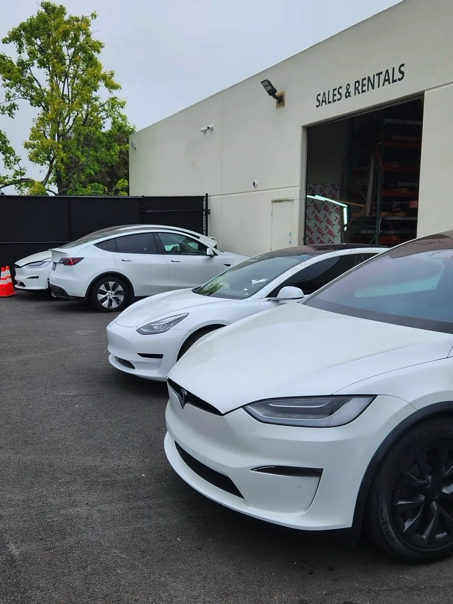 White Tesla Model X and Model 3 vehicles parked outside TSK EV collision repair shop