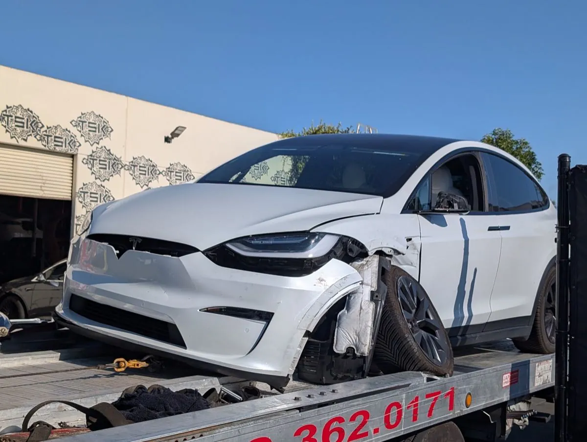 White Tesla Model X with damaged front bumper on tow truck at TSK Irvine