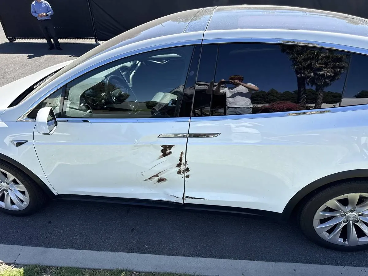 White Tesla Model X with deep scratch and paint damage on rear door panel