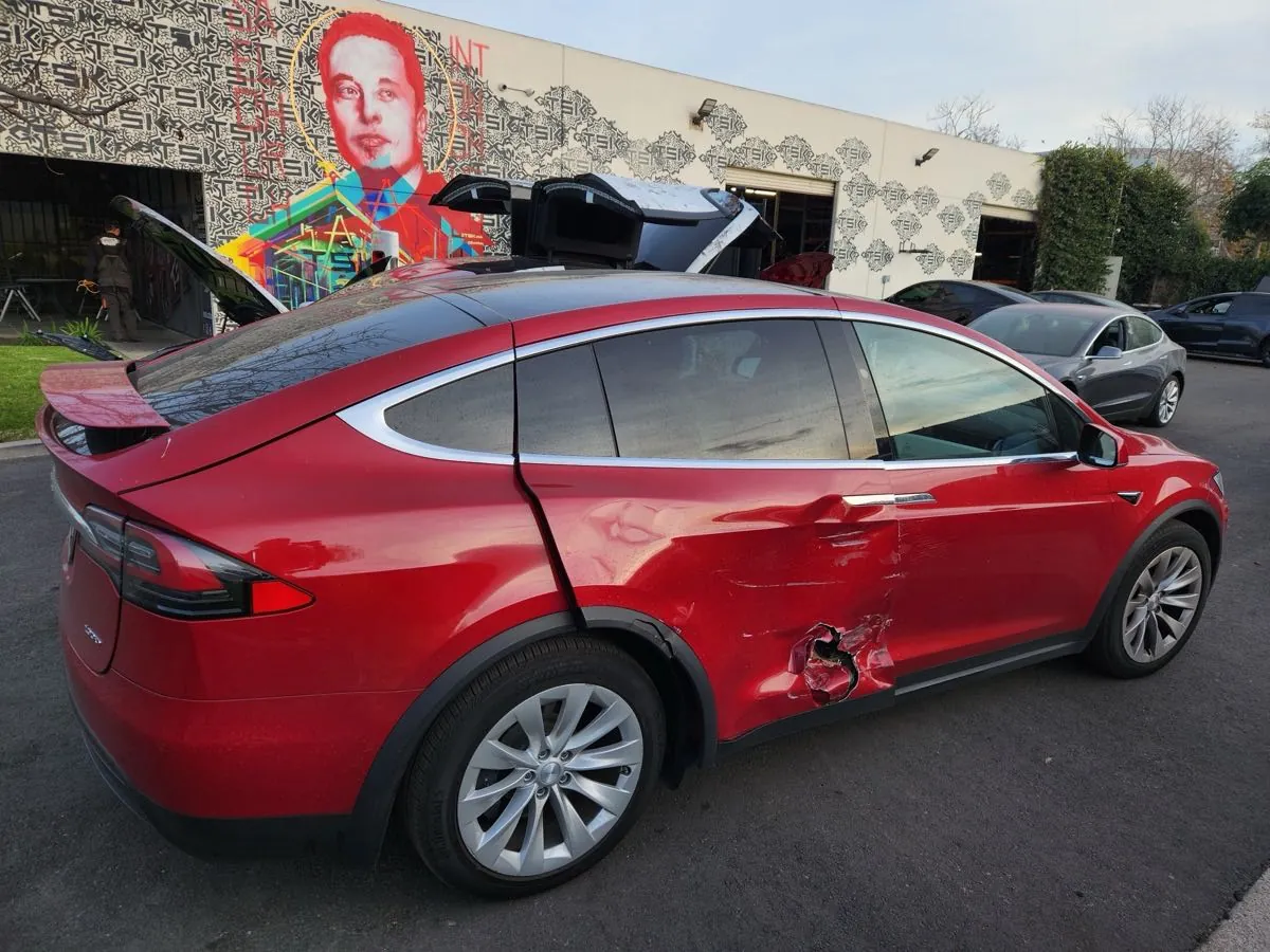 Red Tesla Model X with damaged door and rocker panel at TSK Irvine collision repair shop