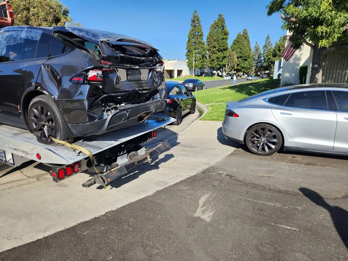Damaged Tesla Model X with crushed rear end loaded on tow truck flatbed
