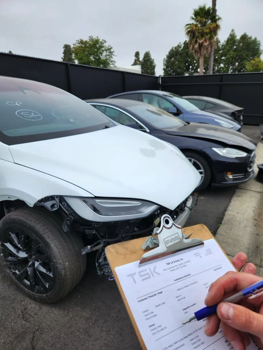 Technician writing preliminary estimate on clipboard beside damaged Tesla Model X front end