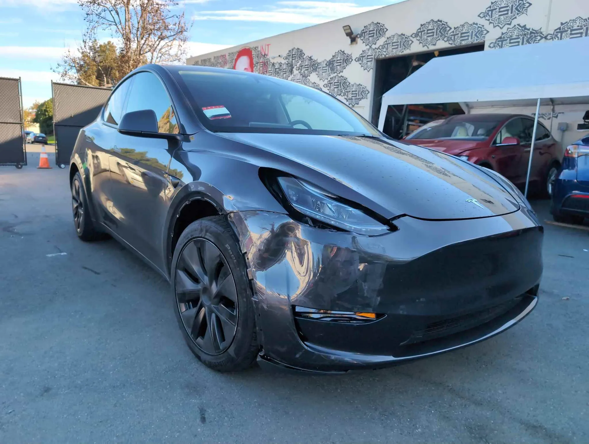 Gray Tesla Model Y with damaged front bumper at TSK collision repair shop in Irvine