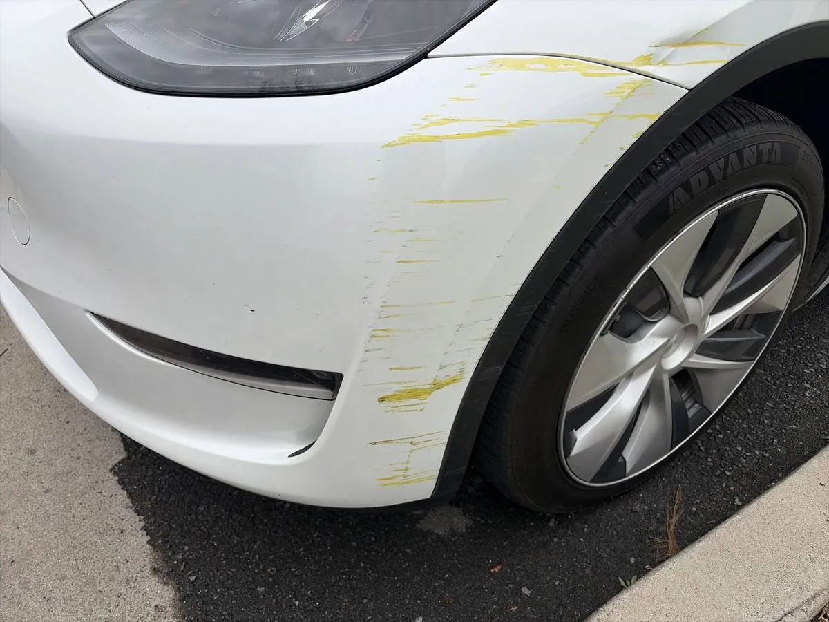 White Tesla Model Y front bumper with yellow paint transfer scrapes before repair