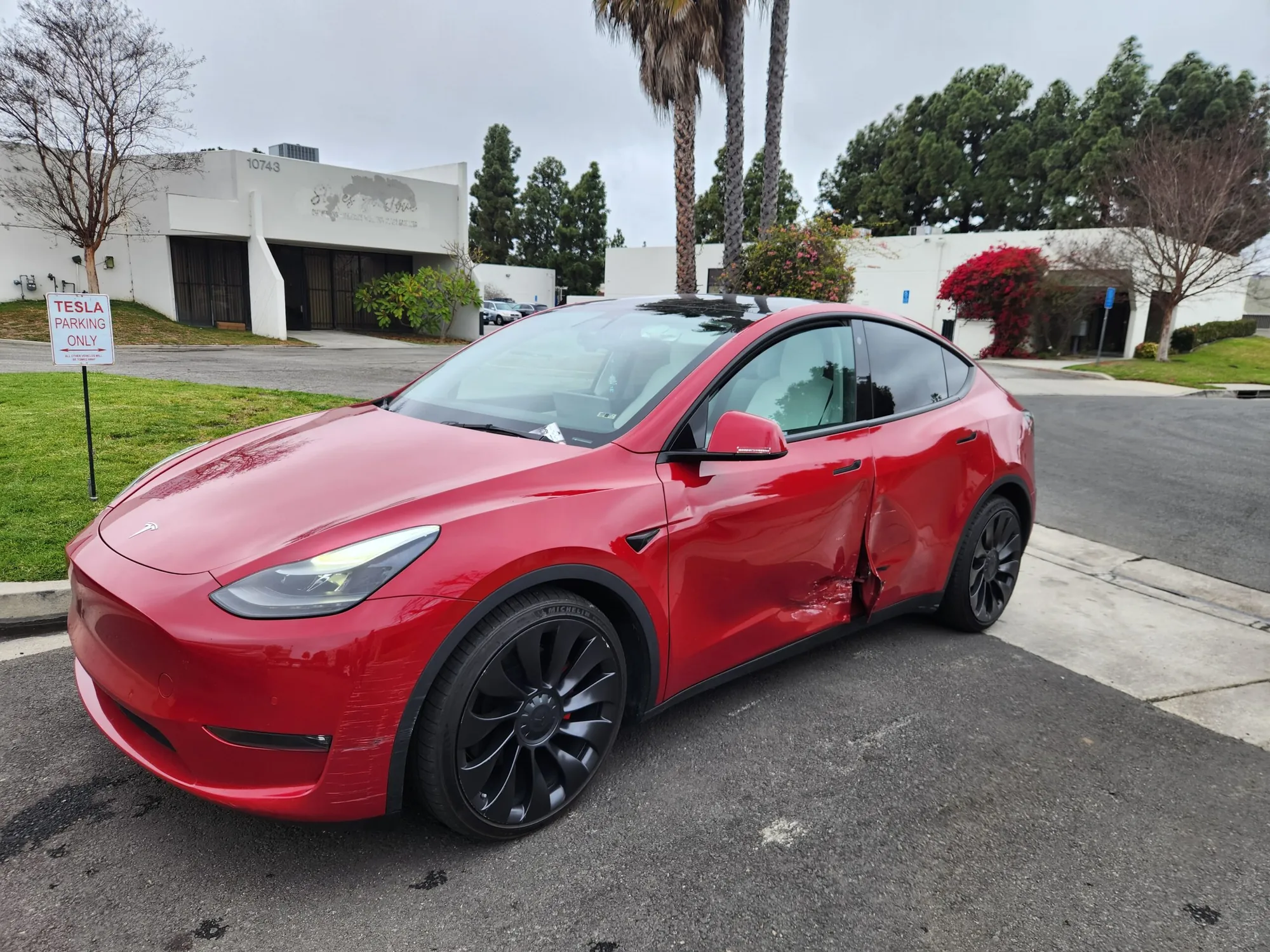 Red Tesla Model Y with rear door collision damage in TSK Irvine parking lot