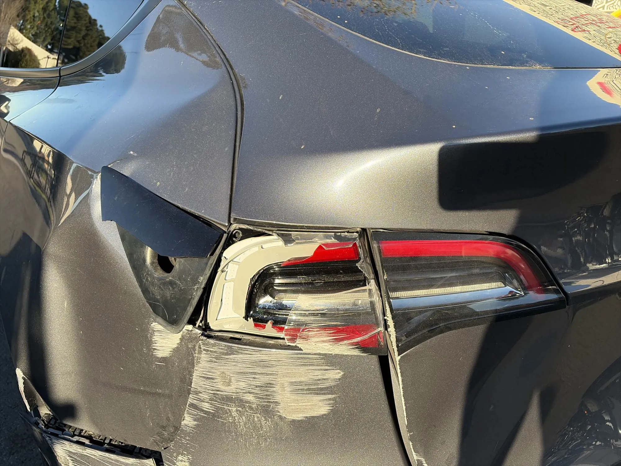 Cracked taillight and scraped rear bumper on gray Tesla Model Y before repair