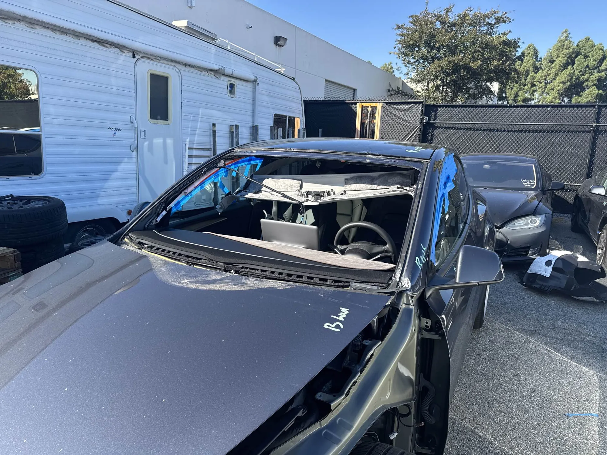 Damaged Tesla Model Y with removed windshield at TSK collision repair yard in Irvine