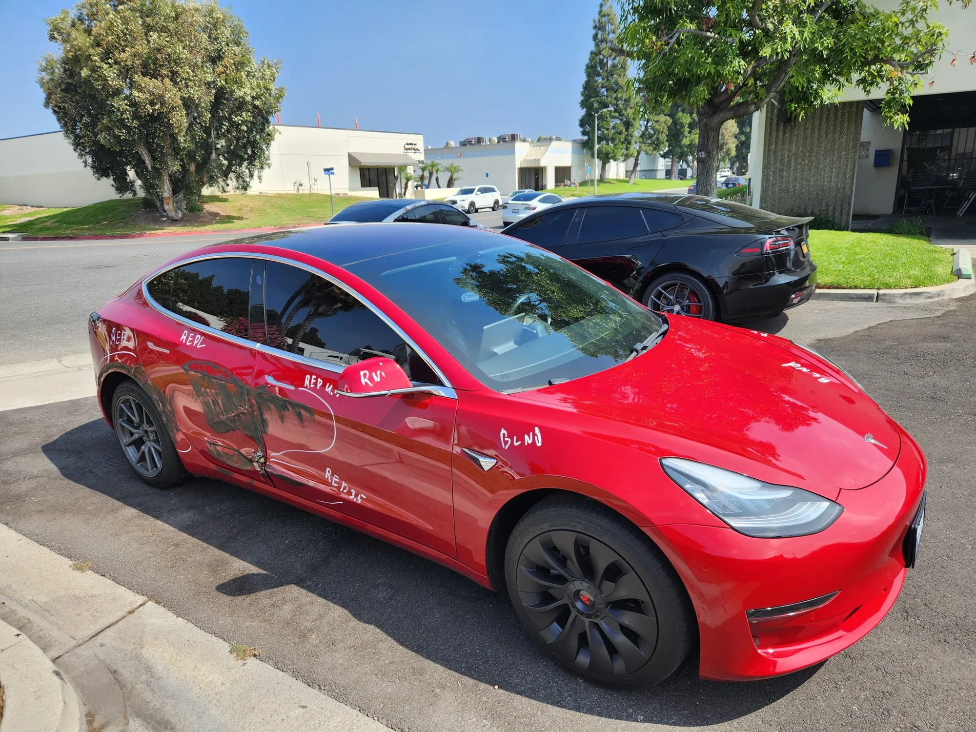 Red Tesla Model 3 with door dent marked for body repair at TSK