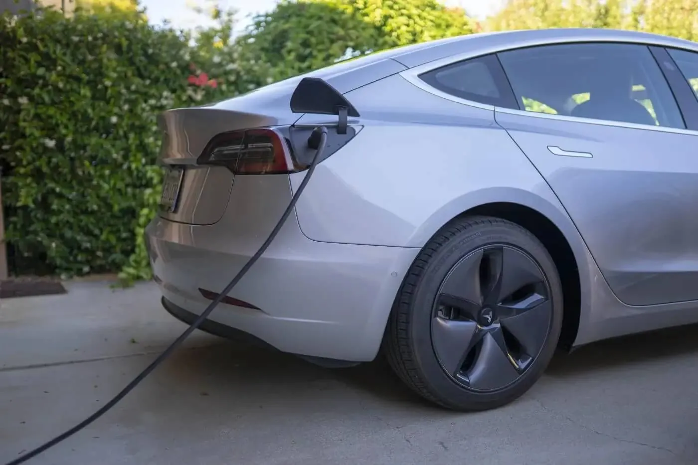 Silver Tesla Model 3 charging in driveway, cable plugged into rear port