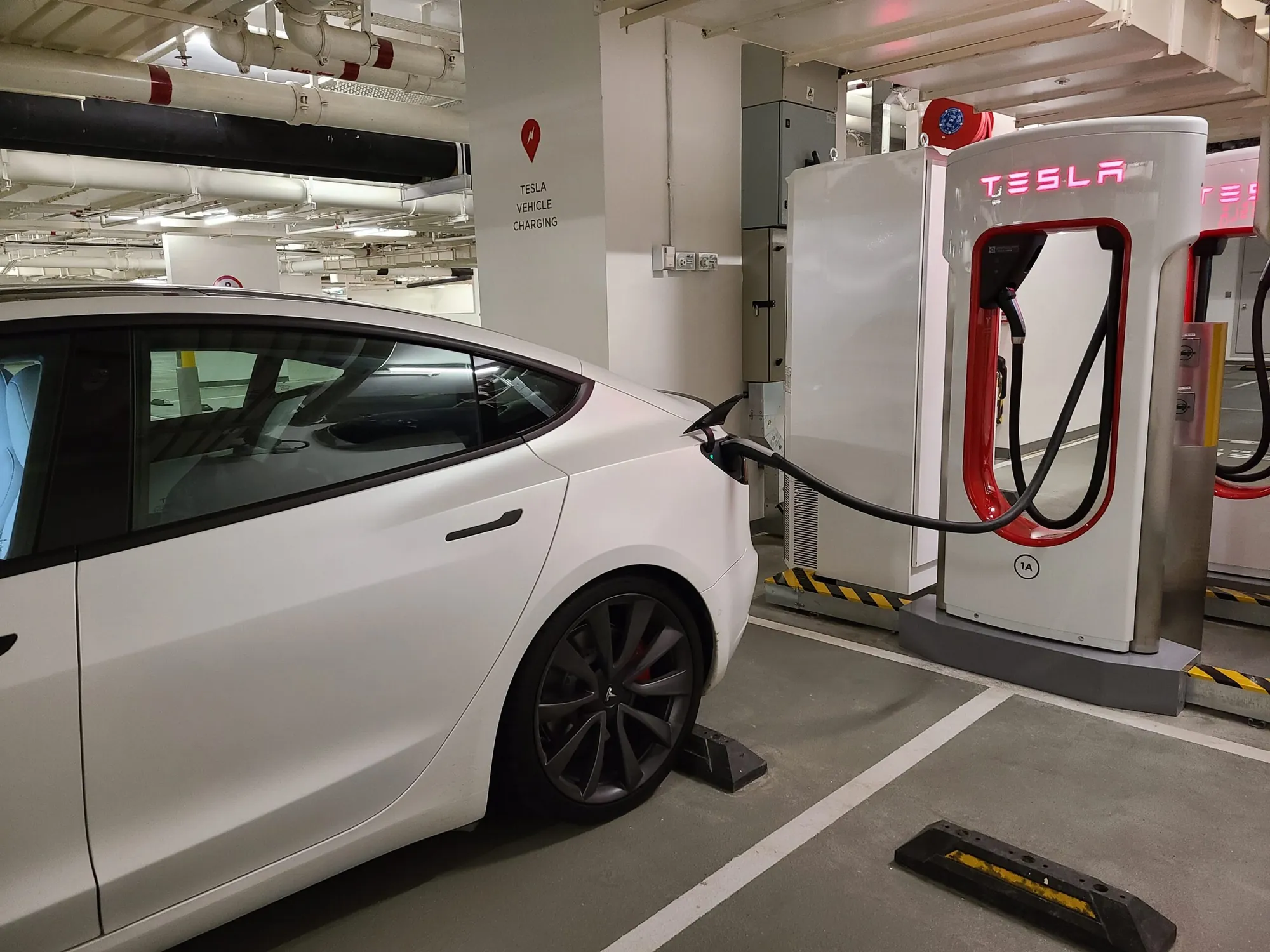 White Tesla Model 3 plugged into Supercharger in parking garage for charging diagnostics